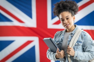 African american female student standing in front of British flag with school bag and notebook.
