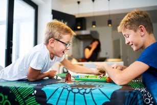 Two brothers laughing playing a board game on the kitchen table