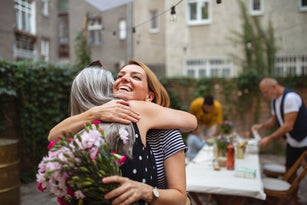 Happy adult daughter with bouquet hugging her senior mother outdoors in garden.