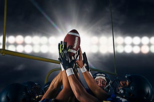 Victorious teenage and young male american football team holding up ball at night