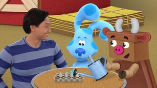 Josh, Blue, and Reusabull are standing next to a table. On the table, there is an empty egg box filled with soil. Tiny seeds are planted inside the soil. Reusabull is pouring water onto the soil.