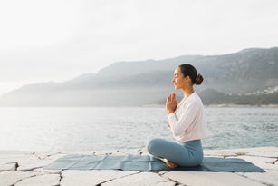 Young woman praying and meditating outdoors by seaside. Self care and mindfulness, menthal health. Awakening in morning