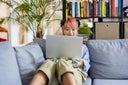 Asian with headphones sitting on sofa working on laptop at office