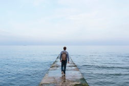 Rear view of a young man with backpack walking towards the sea