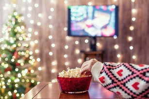 Christmas eve. Alone woman watching tv and eating popcorn. Home cinema. Cropped, close up
