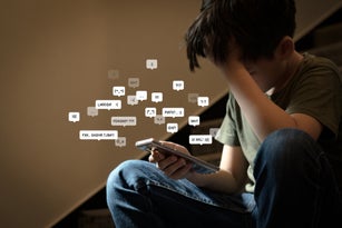 Asian preteen boy sitting at stair, covering his face with hands, face down, holding smartphone in low light.