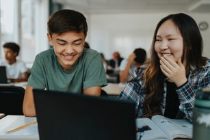 Happy teenage boy and girl using laptop while sitting together in classroom