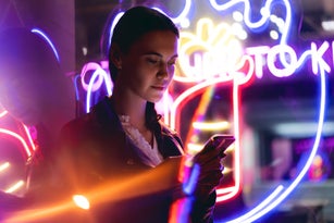 Progressive woman is using mobile phone at night in neon lights