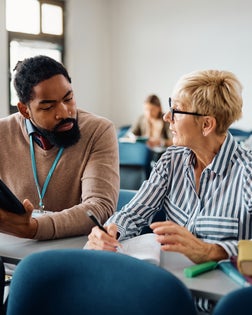 Black adult education teacher assisting mature student with her assignment during a class.