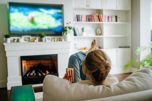 Cozy hugge fireplace and watching TV. Woman eating popcorn and watching tv on a big screen at home