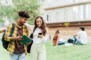 College student couple walking out of class while having fun looking at mobile phone.