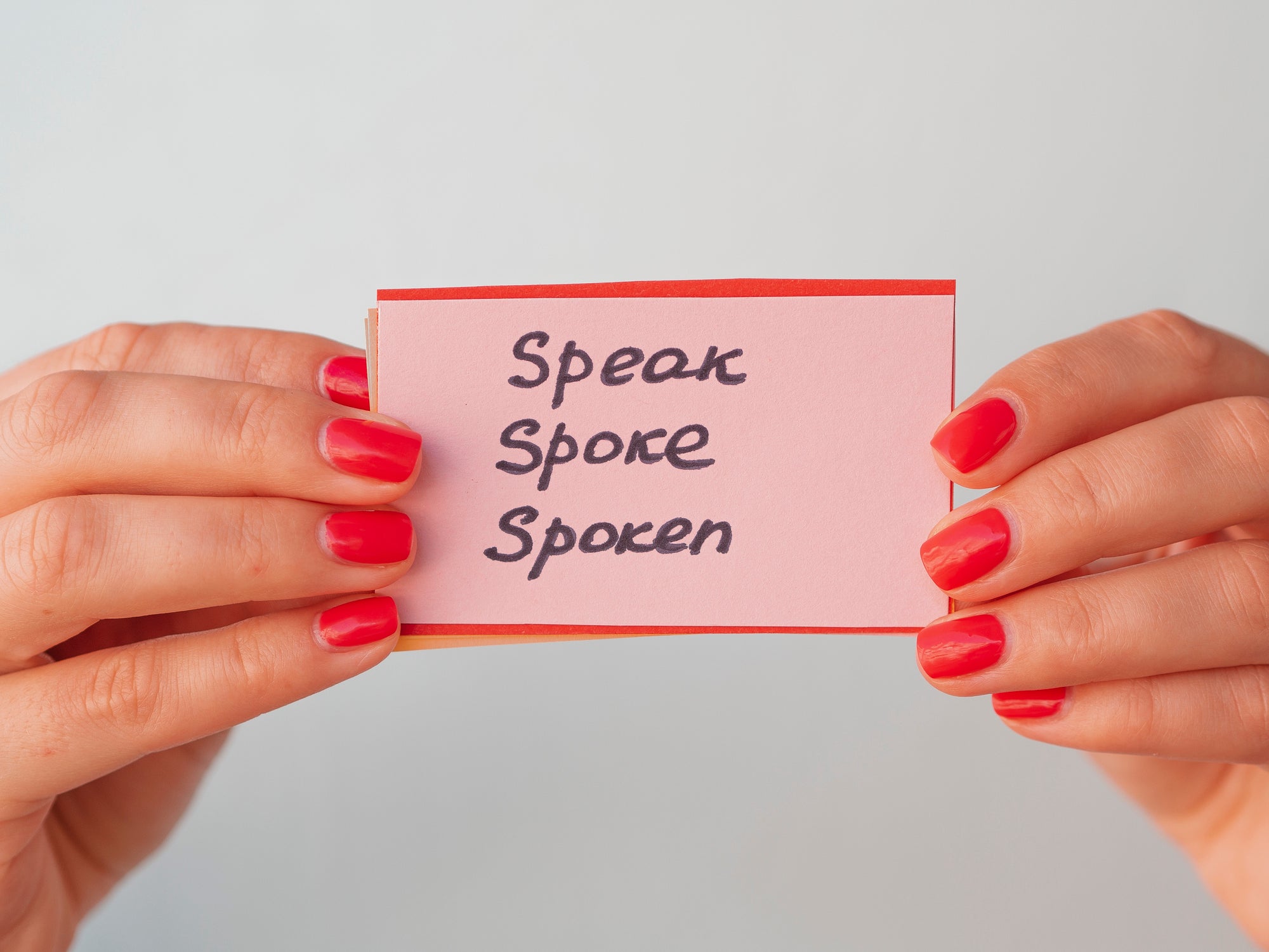 Female hands holds flashcards with handwritten irregular English verbs. Language learning concept