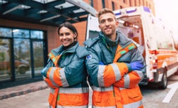 Two confident young doctors looking on the camera on ambulance and hospital background