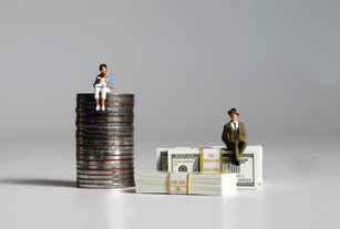 A pile of bills and coins. Miniature people. The concept of wage inequalities according to women's career break.