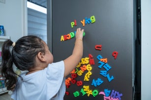 Kid Playing with Magnet Letters Text on Refrigerator