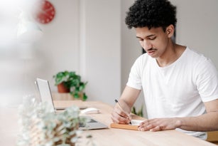 Young man writing in his notebook shopping list on his home