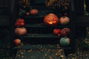 Halloween jack-o'-lantern sitting on porch steps with pumpkins and autumn leaves