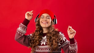 Christmas music. Pretty young woman in headphones and winter outfit dancing to her favorite song on red background