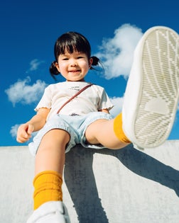 Low angle view of cute little Asian girl smiling joyfully and having fun in outdoor park against beautiful blue sky on a lovely sunny day