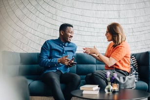 Businessman and woman using mobile phones while sitting on couch during conference