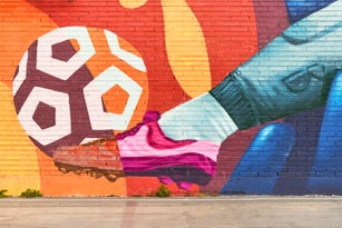 Colorful street art mural depicting a soccer player kicking ball