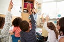 Elementary school kids raising hands to teacher, back view