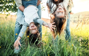 A father and mother holding their daughters upside down outside in spring nature.