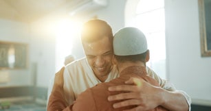 Muslim, religion and people hug in mosque for community, support and greeting Islamic leader. Holy temple, prayer and men in religious building for Ramadan Kareem, Eid Mubarak and praying together