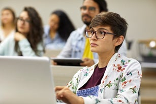 Young student with laptop studying in classroom