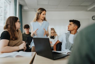 Female teacher gesturing while explaining to teenage boy and girl in classroom