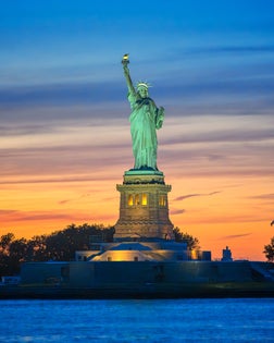 Sunset behind the illuminated Statue of Liberty in New York Harbor