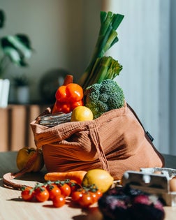 Eco-friendly reusable shopping bag with multi-coloured fresh vegetables and groceries on the table at home. Shopping with reusable grocery bag for plastic free and waste-free life. Responsible shopping. Zero waste and sustainable lifestyle concept