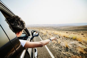 Teenage boy with arm and head out car window during desert road trip
