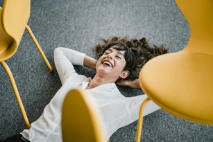Laughing businesswoman laying in an office on the floor between chairs