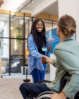 African woman shaking hands with businessman sitting on wheelchair at a conference