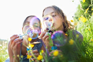 Sisters sitting in field of flower blowing bubbles