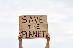 Unrecognizable man's hands holding a protest banner with the message SAVE THE PLANET, with the sky in the background.