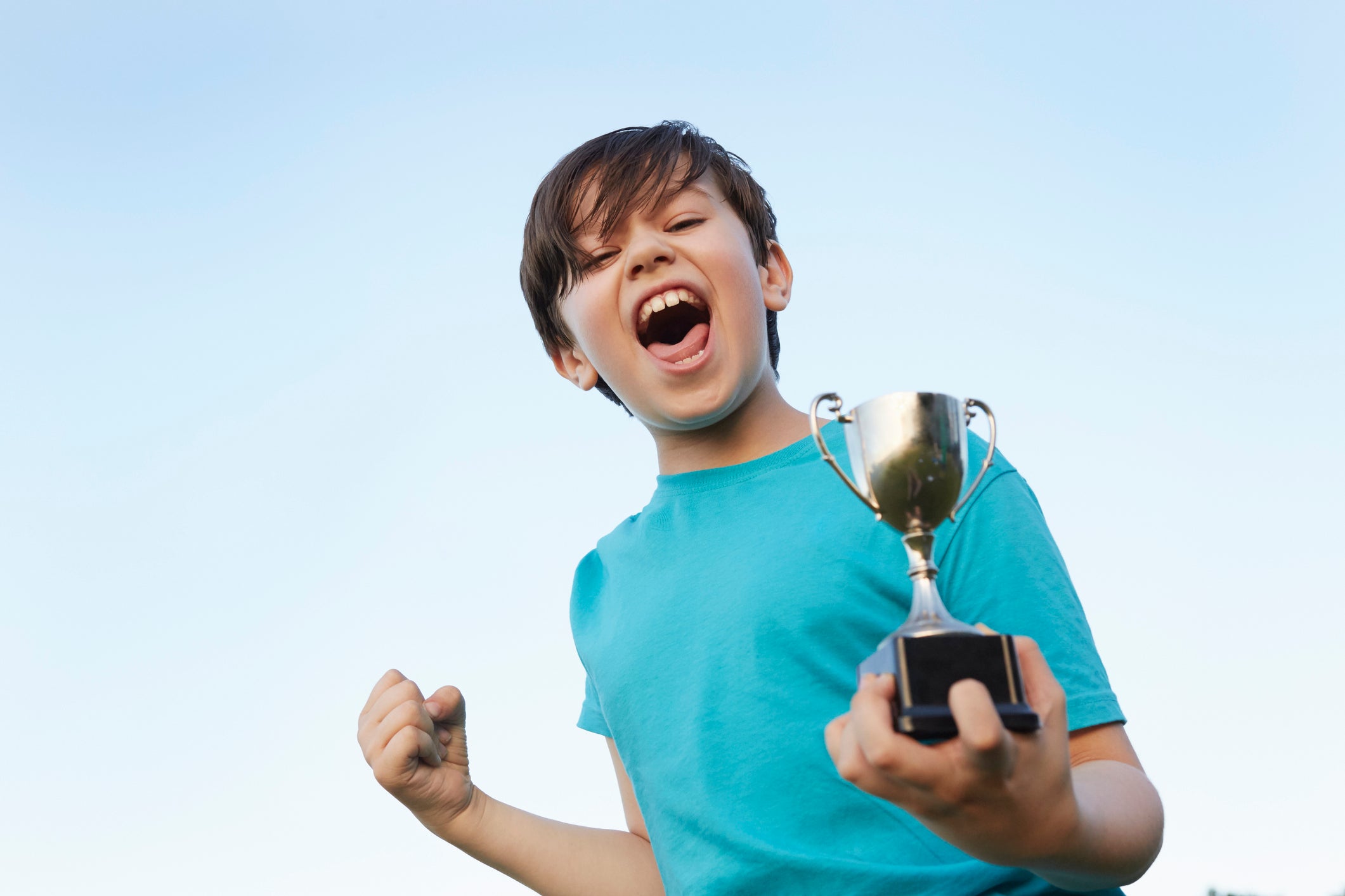 Boy making fist and holding sport trophy against blue sky