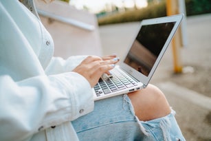 Remote, freelance job and social media online. Cropped hands work on black screen laptop outdoors
