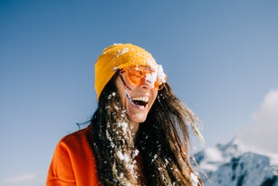 Woman in sunglasses laughs joyfully while playing in the snow in the mountain