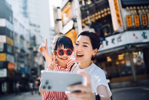 Joyful young Asian mother taking a selfie with her lovely daughter with smartphone while exploring and sightseeing the city in Tokyo. Happy young family having fun and enjoying spending time together. Family travel and vacations