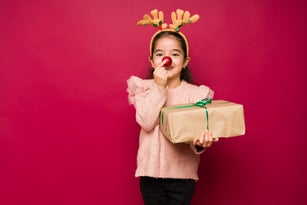 Adorable girl putting up a red reindeer nose for christmas