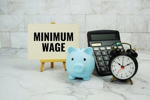 Minimum Wage text written on paper card with piggy saving, calculator and alarm clock on marble background