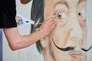 Young man artist draws with paint brush surreal man portrait on white canvas art painting festival