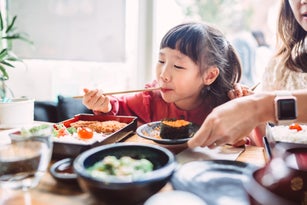 Lovely cheerful girl enjoying meal with her mom in a Japanese restaurant