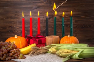 ignition of Kwanzaa traditional candles, holiday concept with gift box, pumpkins, ears of wheat, grapes, corns, banana, bowl and fruits on wooden background, close up