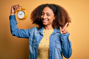 Young african american woman with afro hair holding vintage alarm clock over yellow background surprised with an idea or question pointing finger with happy face, number one