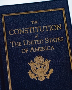 The Constitution of The United States of America book in hand on blurred background.
