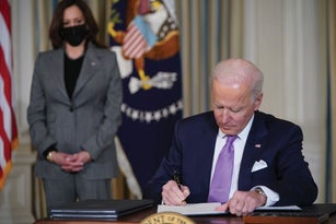 President Biden signs paperwork while Vice President Harris looks on.