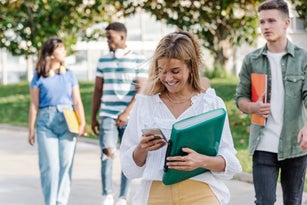 Cheerful young female student using smartphone near friends